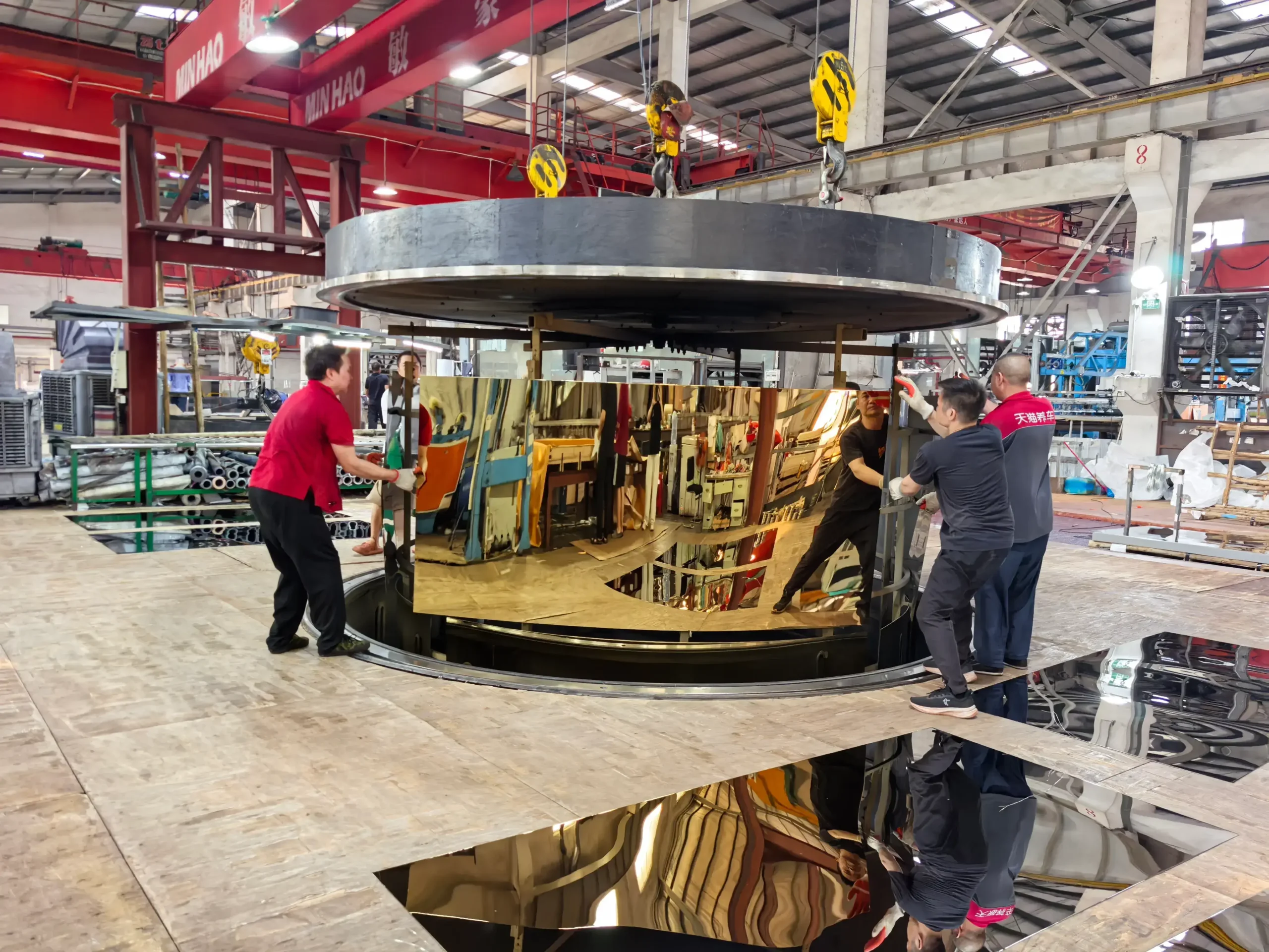 Production team handling a large gold mirror stainless steel sheet beside PVD coating equipment